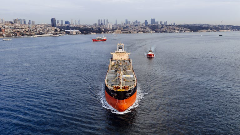 A stunning aerial shot of a cargo ship navigating the Bosphorus Strait in Istanbul, Turkey, with a city skyline.